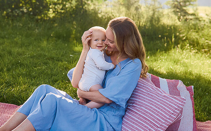 Ein zärtlicher Moment zwischen einer Frau und einem Baby vor einer grünen Kulisse.