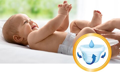 Ein fröhliches Baby, das auf einem Bett liegt, mit einer Nahaufnahme des Windeldesigns im Vordergrund, das die saugfähigen Eigenschaften der Windel hervorhebt.