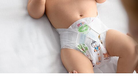 Ein Baby, das eine Windel mit einem Cartoon-Motiv trägt und auf einer weißen Fläche liegt.