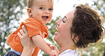 Ein freudiger Moment zwischen einer Mutter und ihrem Baby, in dem die Mutter das Baby hochhält, beide lachen und die Gesellschaft des anderen genießen.