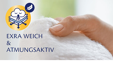 Nahaufnahme eines weißen, flauschigen Materials, das von einer Hand sanft berührt wird, begleitet von einem Text in deutscher Sprache, der übersetzt "Extra schwer und weich" bedeutet, mit einem Wolkensymbol und einem Federsymbol.