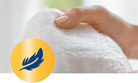 Eine Nahaufnahme einer Hand, die ein weißes, flauschiges Objekt hält, mit einem blauen Federsymbol in einem gelben Kreis darunter.