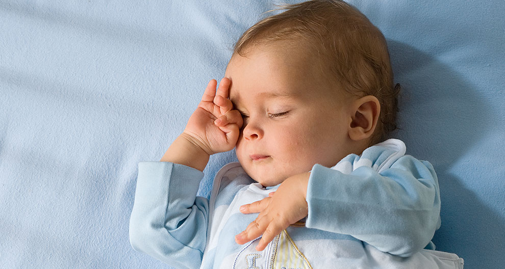 Ein Baby, das scheinbar tief schläft und dessen Gesicht von einer Hand sanft berührt wird.