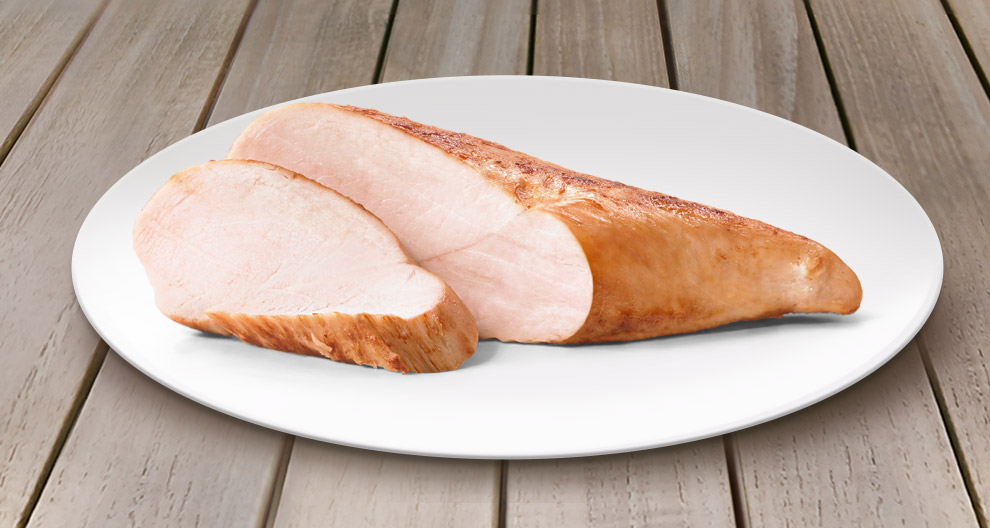 Ein in Scheiben geschnittenes Stück Fleisch, vermutlich Truthahn, auf einem weißen Teller vor einem hölzernen Hintergrund.