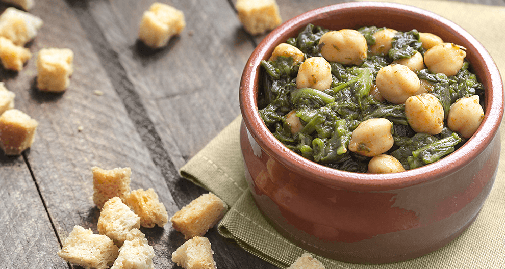 Eine Schüssel mit Kichererbsen, gemischt mit grünem Blattgemüse, dazu Croutons, die in der Schüssel verstreut sind.